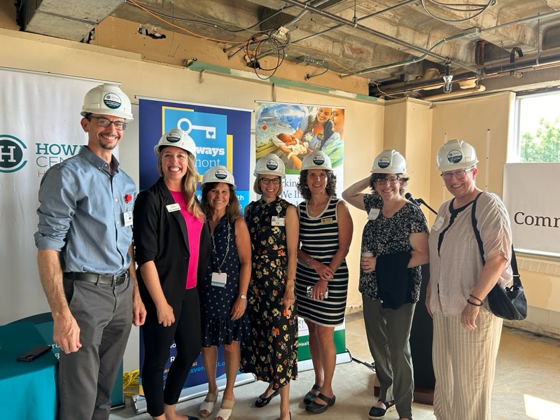 A group of people stand together in front of standing banners. There are 7 people total and they are all wearing hard hats