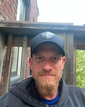 Selfie of a man with a beard wearing a baseball hat and sweatshirt